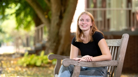 Ella sits on a bench on campus